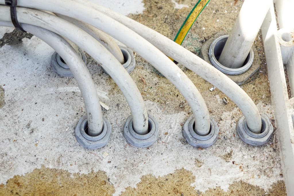 Close-up detail of wires in tubing and a fuse box along a white ceiling and wall. Interior design concept